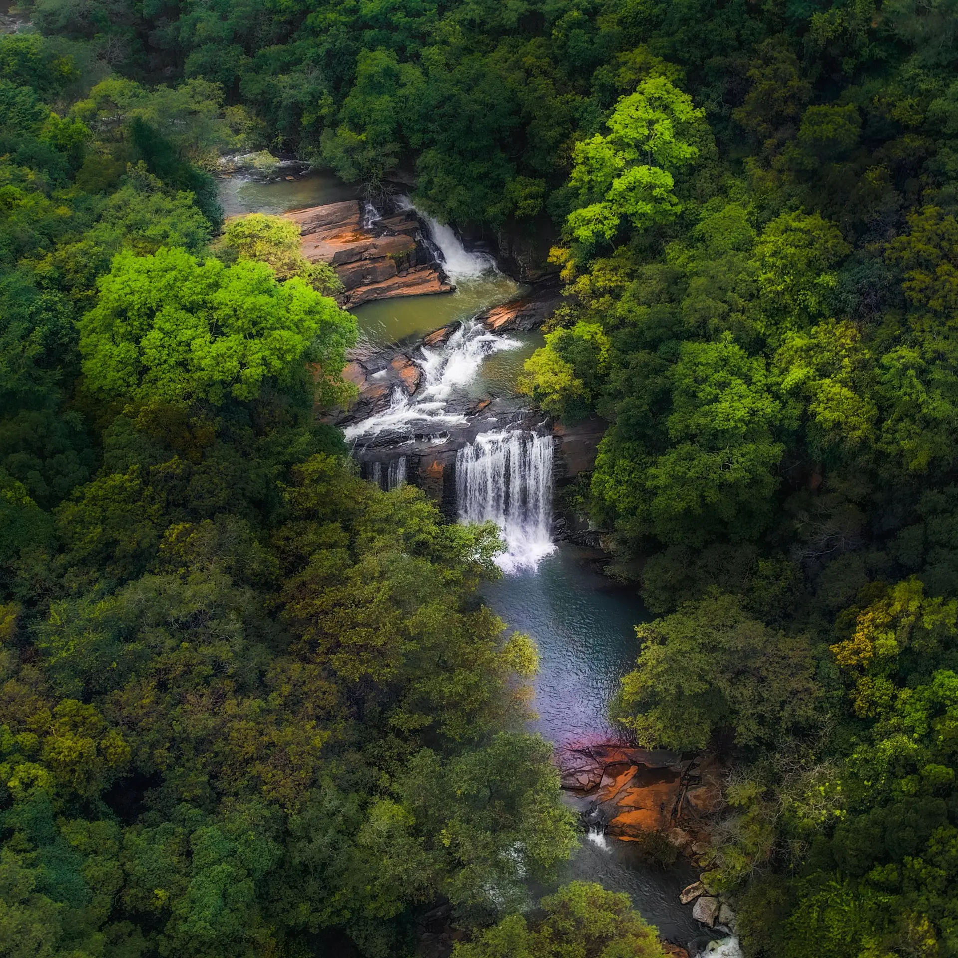 Aerial view of waterfalls threading down a forested hillside.